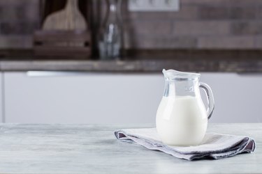 a glass pitcher of milk on a gray napkin on a marble countertop