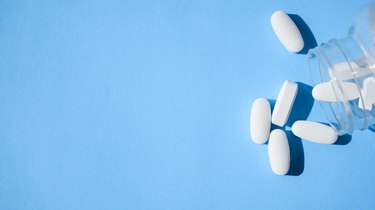 White vitamin pills pouring out of a glass bottle onto a blue background