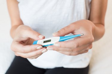 Close up of a young adult holding a blue and white digital thermometer, measuring their low body temperature